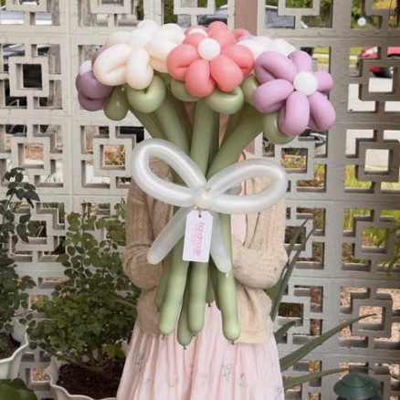 Pink and white balloon daisies with a large white bow in front of a breeze-block wall.