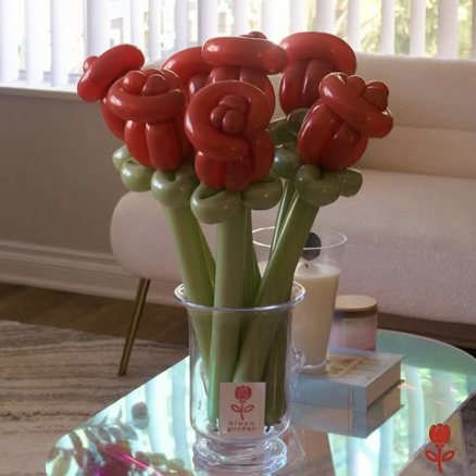 Deep red balloon roses standing in a glass vase on a side table.